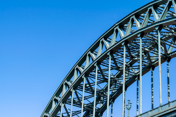 A portion of the Tyne Bridge, at a dynamic angle, featured at the bottom right hand section of the image contrasting against a beautiful blue sky.
