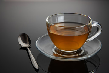 Glass cup of tea on a glass saucer with reflection, with a gradient of black and gray background. Concept, healthy and stylish lifestyle.