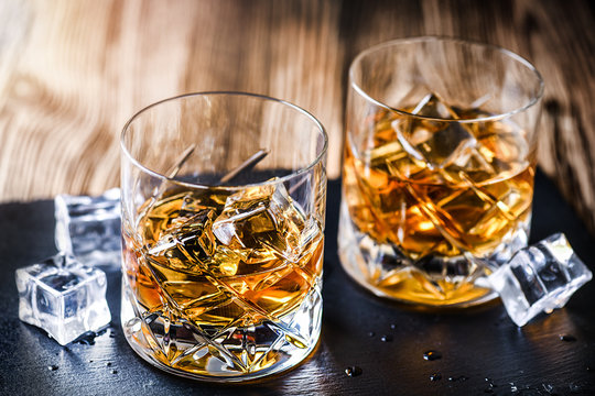 Glass of whiskey with ice cubes on black stone table. Side view with copy space alcohol concept.