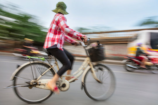Motion blurred photograph of a Vietnamese woman cycling on a bicycle on the streets of Vietnam, South East Asia