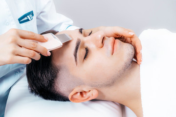 Ultrasonic cleaning of the face. Photo of a young man on a facial cleansing procedure in a cosmetology clinic.