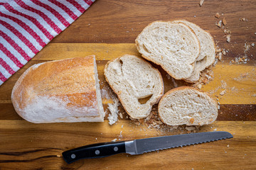 Freshly baked Italian Bread, sliced with a serrated bread knife on a wooden cutting board with a red and white towel