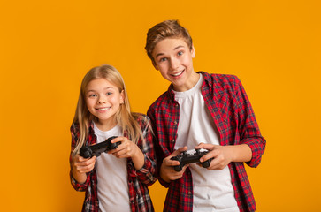 Kids Leisure. Brother And Sister With Joysticks Posing Over Yellow Background © Prostock-studio