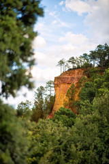 Vertical picture of hiking path Ochre Trail in a natural colorful area of orange cliffs surrounded by green forest in Roussillon, one of the most beautiful villages of France, Provence