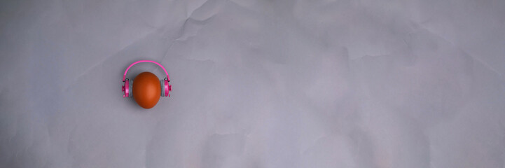 Easter egg with pink headphones on gray background with copyspace. Banner of macro moody minimalistic decoration concept. Stock photo.
