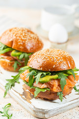 Burger sandwich with salmon, cream cheese, avocado and arugula on a light background, concept diet food, take away, healthy fast food
