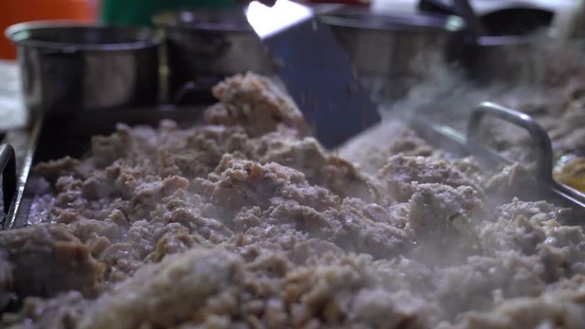Vendor spreading meat guts with spatula across the griddle in preparation for tacos