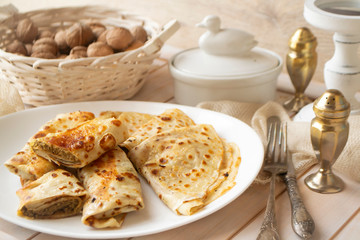rolled up Crepes stuffed with minced liver on white plate on old wooden table with vintage fork and knife