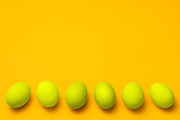 yellow colored eggs in a row on yellow background with copyspace