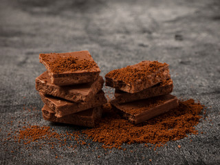Broken pieces of chocolate sprinkled with coffee powder close up.