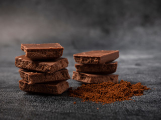 Broken pieces of chocolate sprinkled with coffee powder close up on gray stone background.