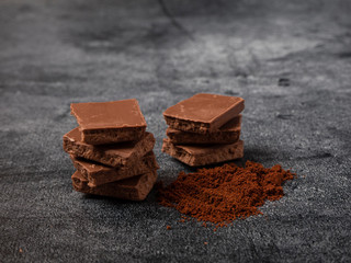 Broken pieces of chocolate sprinkled with coffee powder close up on gray stone background.