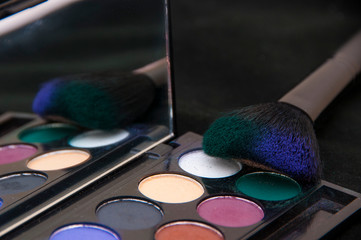 Close up of a multicolored eye shadow and a brush for applying makeup. Beauty products on the black background.
