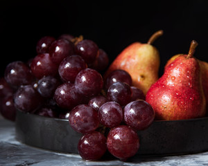 bunch of purple grapes and ripe red pear fruits on plate