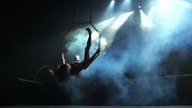 Slim and sexy female Aerial acrobat on the stage with aerial hoop with spot lights on background 