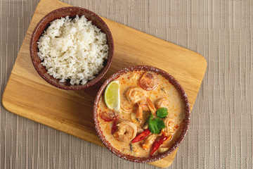Ceramic bowl of Thomas soup with shrimp and coconut milk and a bowl of rice on the background of wooden boards and a gray mat. Asian food. Top view.