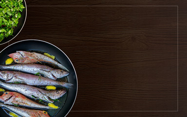 The concept of simple healthy food. Fresh sea fish in olive oil prepared for frying in a pan with herbs and lemon and spinach on a black wooden background. Mediterranean diet. Food photo