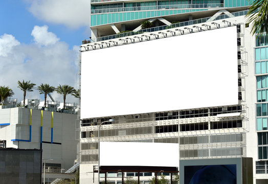 Large and small billboards on side of building wall. Modern city, palm trees, blank ad space. Banner edge and grommets preserved for a more realistic look. Clipping path included.