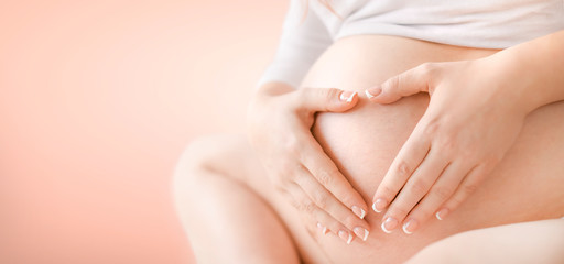 Pregnant woman belly detail isolated on pink Background. Pregnancy tummy concept wide banner or copy space for text.