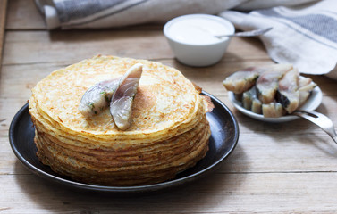Pancakes with glavraks from mackerel and sour cream on a wooden background.