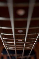 Brown fretboard of a bass guitar. Four metal strings and metal frets. Musical instrument. Low and dense sound. Blurred background.
