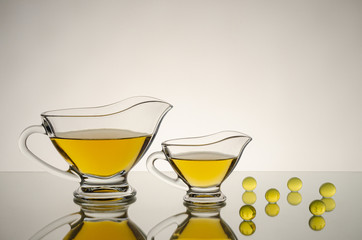 Two glass saucers of different sizes with yellow sauce, on a glossy surface with reflections, next to yellow transparent balls.