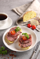 Lunch. Sandwiches with sausage and a cup of coffee on a light grey background. Tomatoes, garlic, white bread, parsley, knife and spices. Background image, copy space