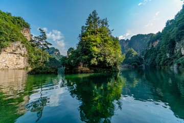 Small island covered with vegetation in the center of a lake with green waters and rugged mountains in the background. Baofeng Lake (Bao Feng Hu) in Suoxi Valley, Wulingyuan, China