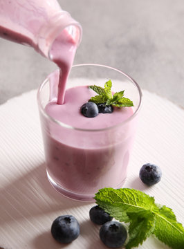 Breakfast. Drinking berry yogurt in a glass on a light board. Fresh berries and mint on a light background. Yogurt is poured from a bottle. Background image, copy space