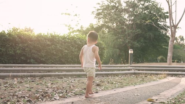 Slow motion video of a Cute little Asian kid Wearing summer clothes walking alone at the park at sunset