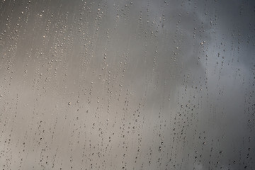 shinny rain droplets on a window, dark clouds in the background