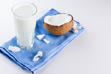 Coconut milk and coconut in glass on white background. Coconut vegan milk non dairy on blue napkin. Healthy drink concept. Minimalism. Alternative milk. Copy space