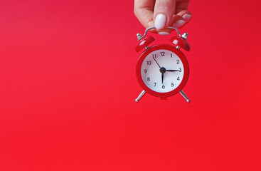 Red alarm clock in female hand on a red background. Copy space.