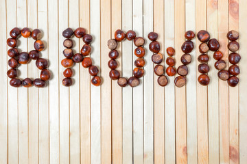 Word brown is laid out with ripe large shiny chestnuts close up on light wooden background top view with copy space and place for text, design