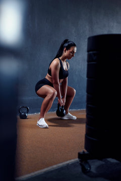 Woman fitness model make workout with weights - squat with kettlebell. Tanned sporty female, with athletic figure. Vertical portrait of sportswoman.