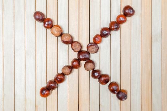Letter X or multiplication sign is laid out with ripe large chestnuts in close up on light wooden background. Flat lay