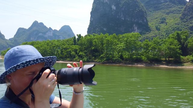 Western female tourist photographing the stuning karst scenery on a trip on the magnificent Li river from Guilin to Yangshuo, China