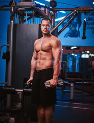 Naklejka premium Strong muscled sportsman doing excersises with dumbbells in a gym looking calm