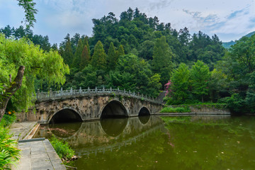 Fototapeta na wymiar Old stone bridge to cross a green lake. Near Purple Cloud Palace in Wudang Shan Mountains, Hubei province, China