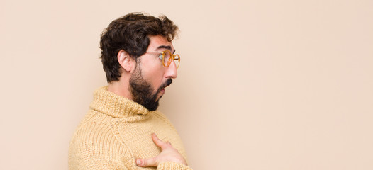 young cool man feeling shocked, astonished and surprised, with hand on chest and open mouth, saying...
