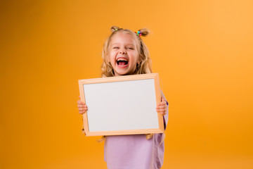 child girl holds a white empty drawing Board on a yellow background, space for text
