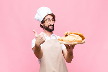 young crazy baker man holding bread against pink wall
