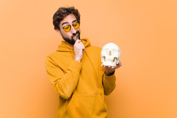 young crazy cool man holding a human skull model against orange wall