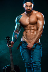 Strong and fit man bodybuilder with guitrar shows abdominal muscles. Sporty muscular guy athlete....