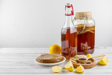 Kombucha superfood pro biotic tea fungus beverage in glass bottle and jar with lemon, ginger, tea on white background