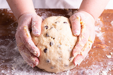 Woman kneading chocolate cookie dough on wooden board with roller ball