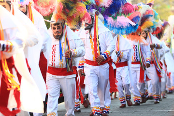 group of males huehue dancers with white pants, shirt and hat with colorful plumes