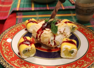 A meringue and fruit roll with whipped cream surrounded by fruit rolls lying on a bright platter cuts with a knife.  