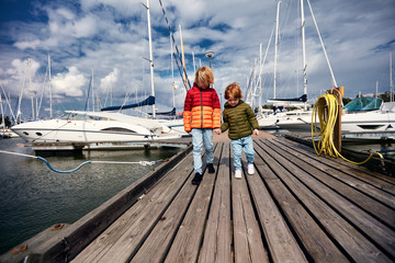 cute kids are walking among the yachts and boats moored in harbor, yacht club