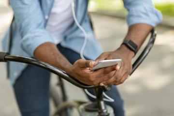 Unrecognizable man on bicycle holding smartphone and listening music in earphones